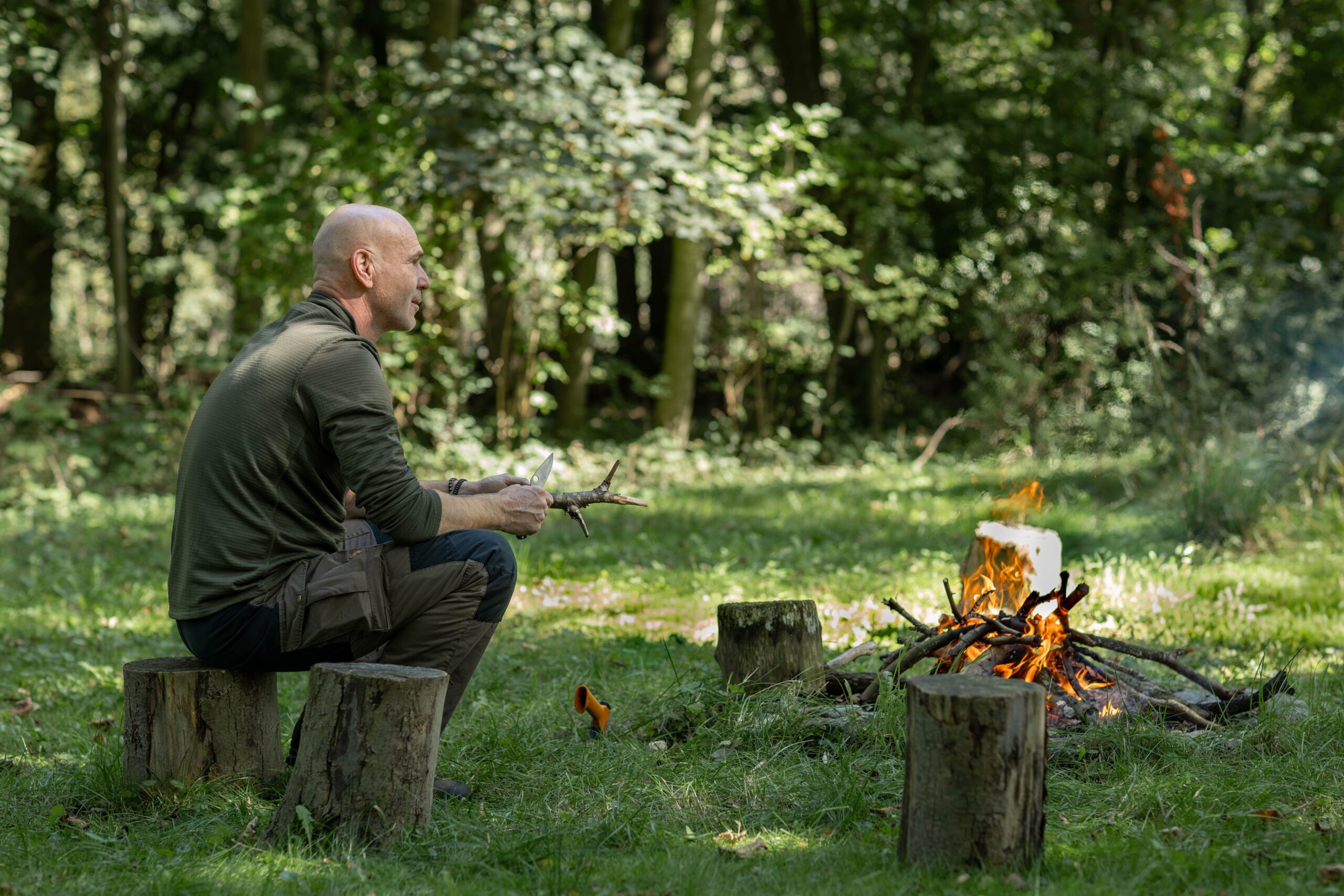 Hans zit op een boomstronk bij het kampvuur in het bos